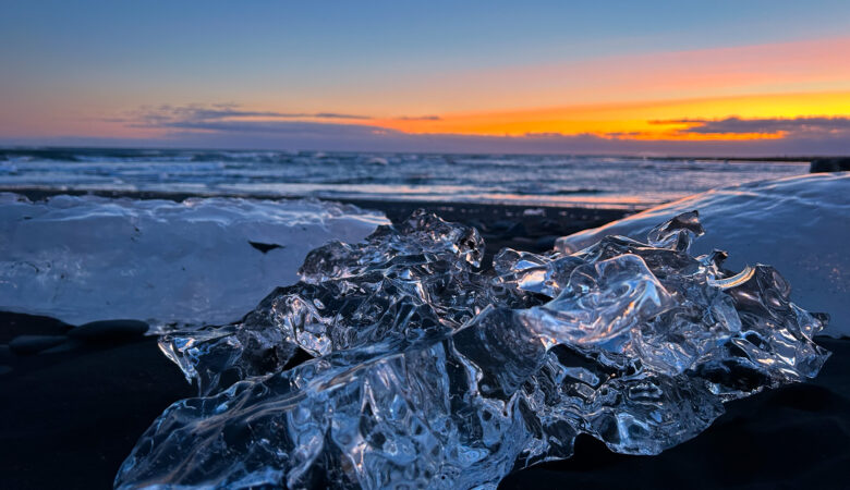 Schwarzer Strand in Island mit angeschwemmtem Eisbrocken vor dem Sonnenuntergang im Winter