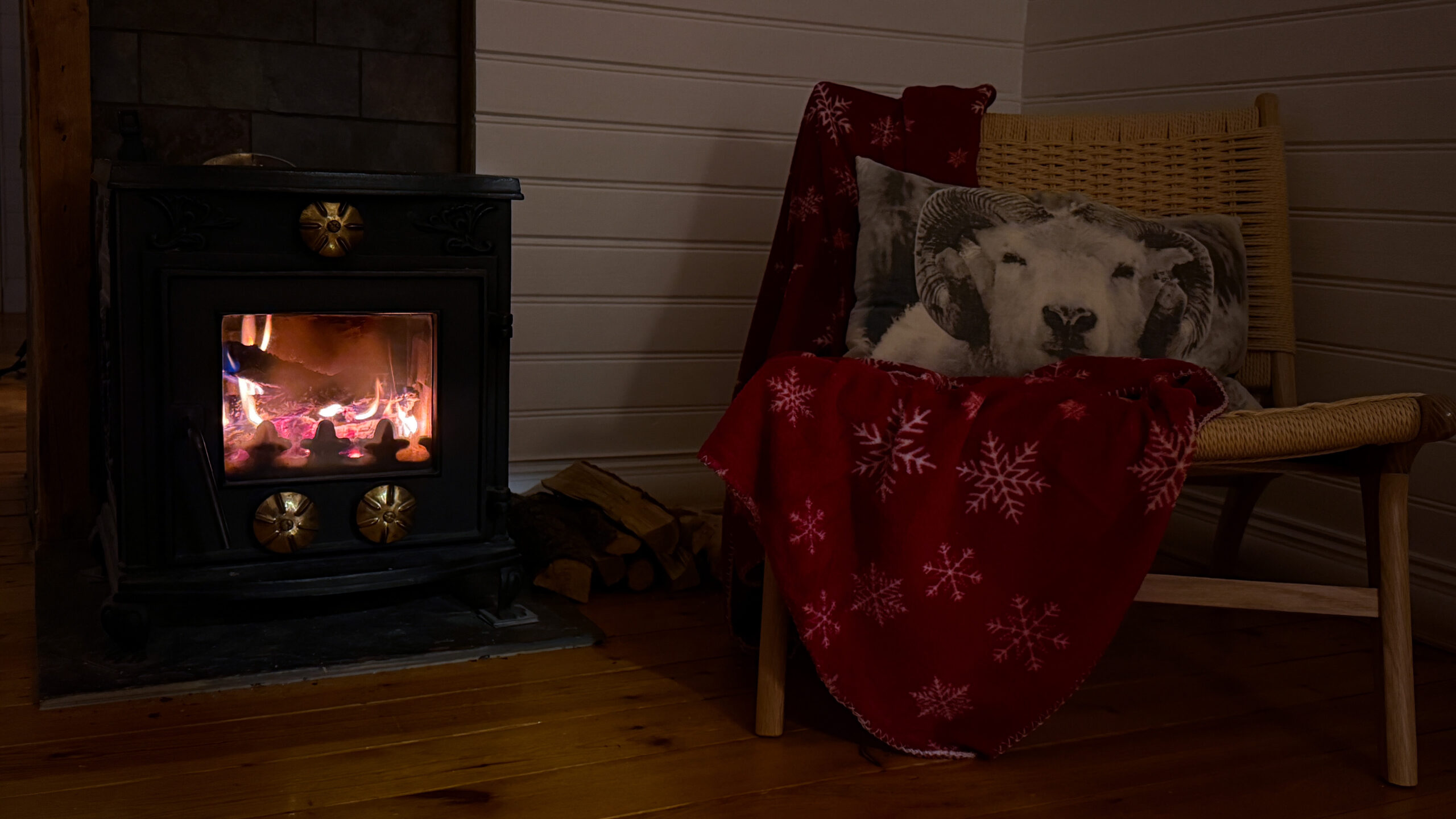 Brennendes Feuer im Kamin neben Sessel mit Decke