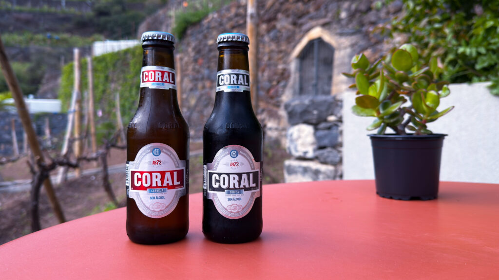 Zwei Bierflaschen stehen auf einem roten Tisch, dahinter ist ein schöner Garten