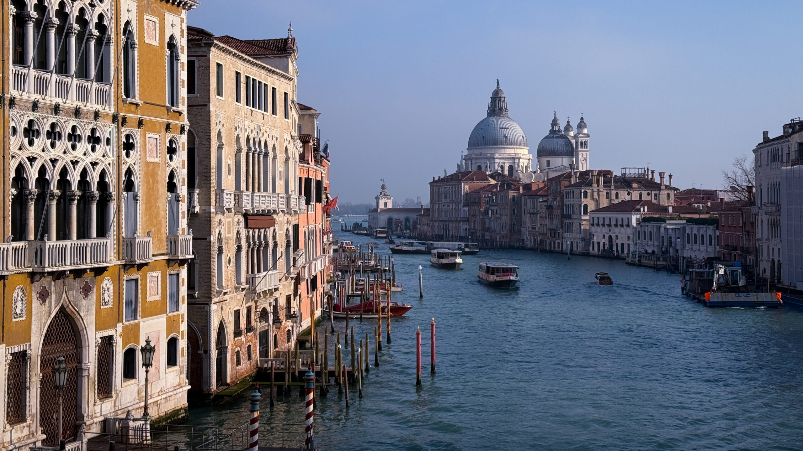 Blick auf den Canal Grande im Sonnenlicht, beleuchtete bunte Häuser im Vordergrund, außerdem Schiffe