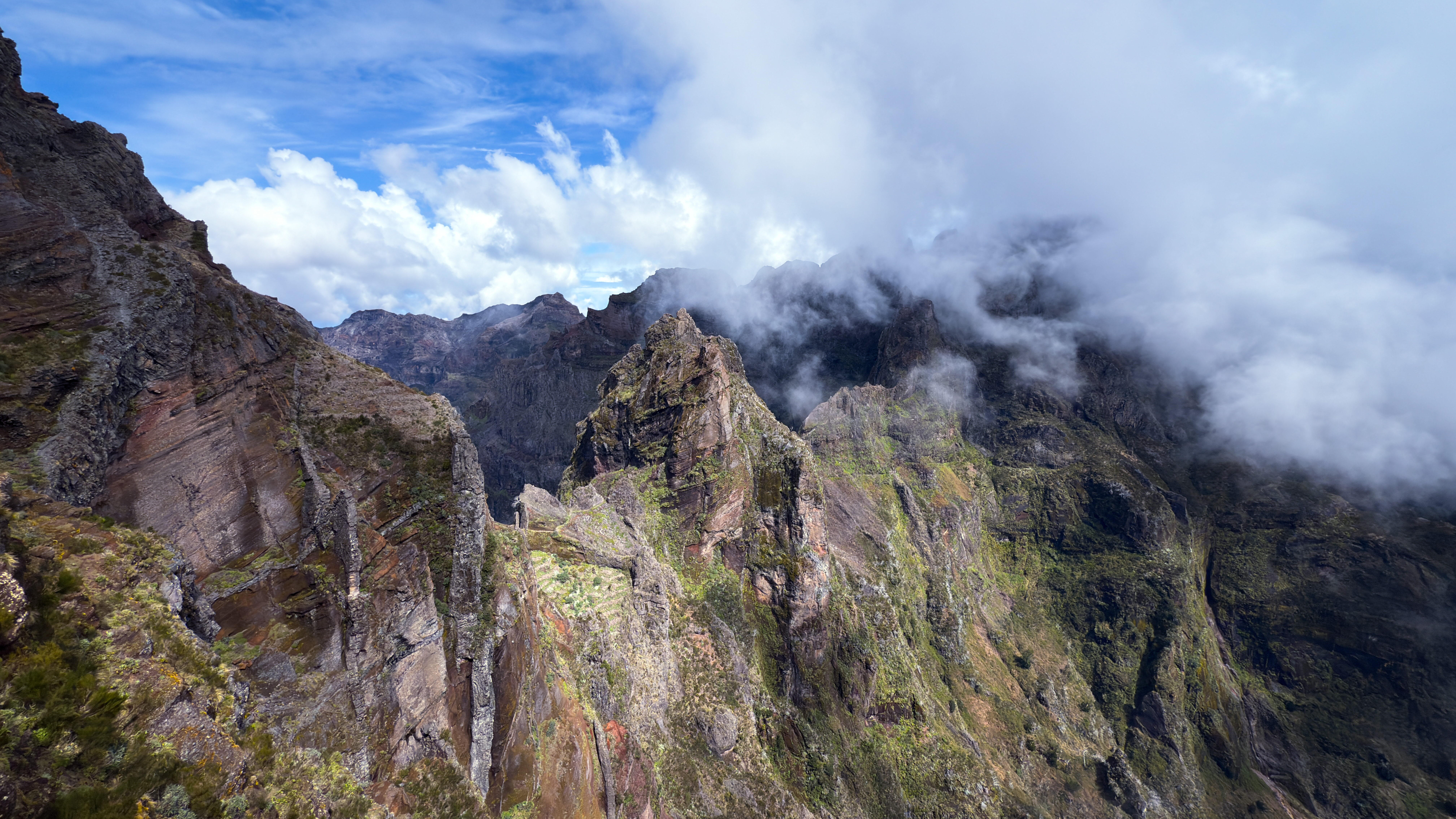 Ausblick von der Wanderung ab dem Pico do Areeiro: Oben blauer Himmel, der von weißen Wolken durchzogen ist, unten graue Berge.