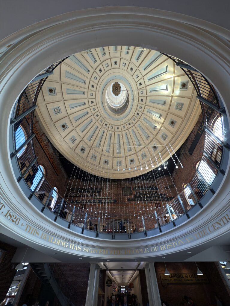 Blick in eine kunstvoll verzierte Kuppel einer Markthalle. Goldene Schrift ziert den Kuppelrand.