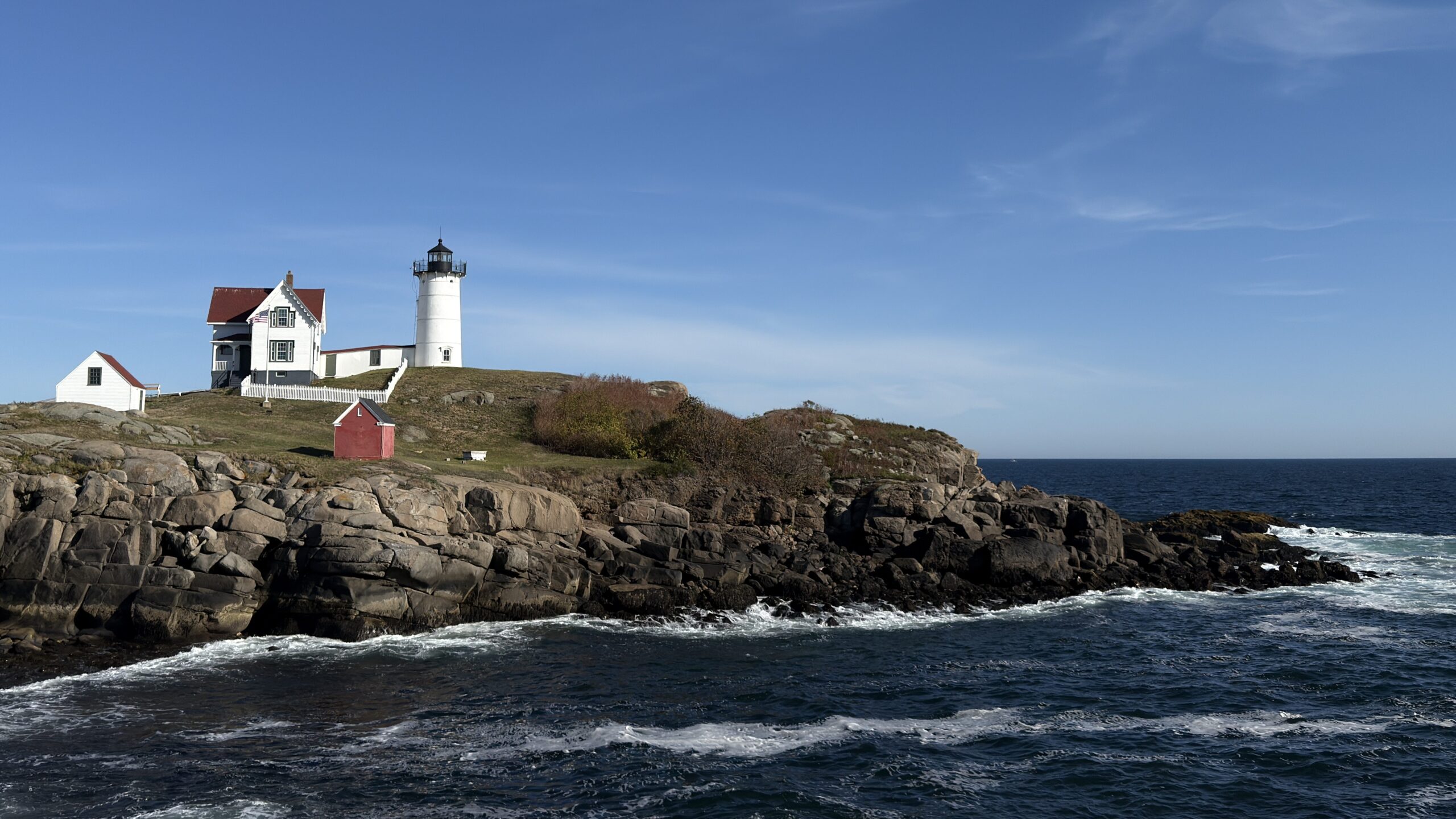 Blick auf einen weißen Leuchtturm, der auf einem Felsen vor dem Atlantik steht. Brausendes Meer.