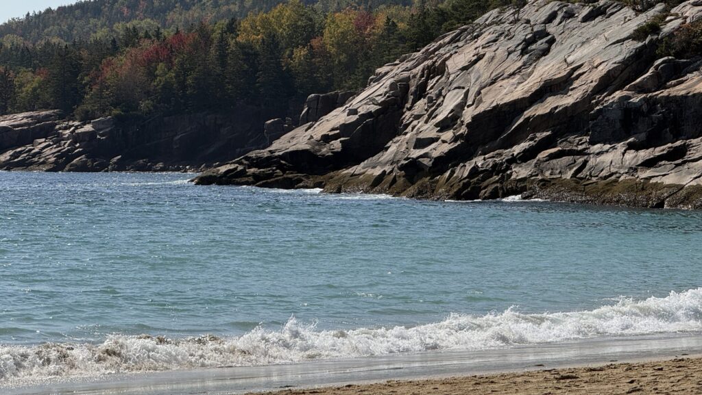 Sandstrand im Hintergrund Felsen und bunt gefärbte Bäume
