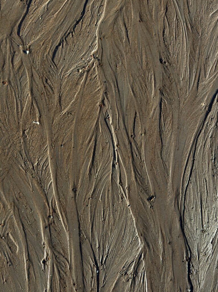 Sand bei Ebbe, mit Mustern des sich zurückziehenden Wassers.